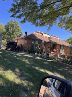 Residential roofing maintenance on a sunny day, with ladders propped up against a single-story brick house as local roofers make repairs.