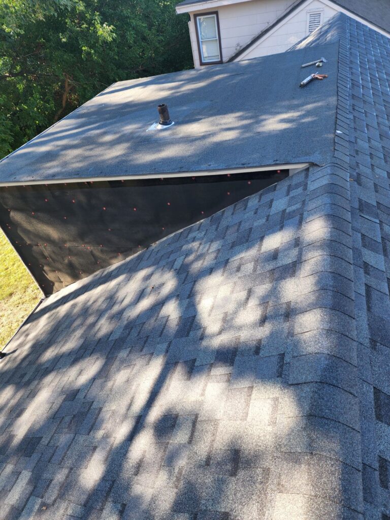 Sunny day casting shadows on a house with a newly installed shingled roof by Kansas City roofers, featuring vents and neat rows of roofing nails ready for the final layer of shingles.